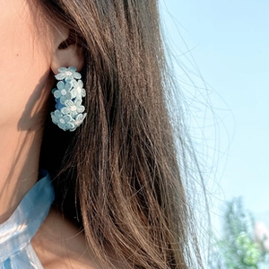 Gros plan d'un modèle portant des boucles d'oreilles en tissu bleu clair sous un ciel azur