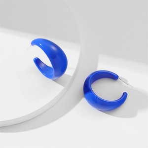 Close-up of bold Klein blue C-shaped acrylic earrings on a white minimalist display