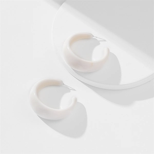 Close-up of thick C-shaped ivory acrylic earrings with subtle marble texture on a white stand