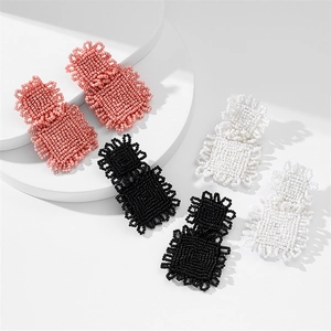Detailed view of handmade beaded square earrings in pink, black, and white on white blocks