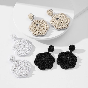 Detailed view of handmade woven flower beaded earrings in beige, white, and black