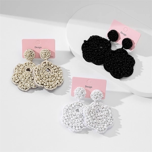 Close-up of handmade woven floral seed bead earrings in ivory, black and white