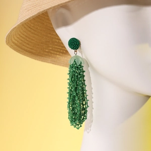 Close-up of green beaded tassel earrings on a model with a straw hat for summer vibe