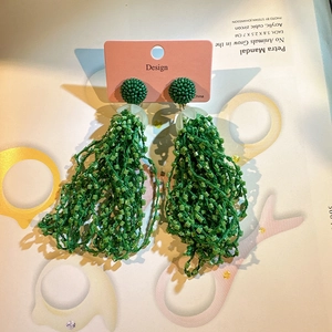 Detail of green seed bead tassel earrings with domed beaded studs on a pink design card