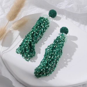 Detail of green handmade seed bead tassel earrings on white ceramic display plate