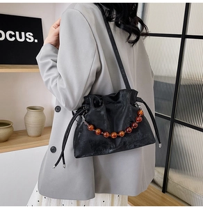 Detail of black pleated cloud bag featuring orange bead chain and matte leather texture