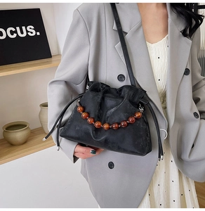 Detail of black drawstring bucket bag with amber beaded chain and vintage leather texture