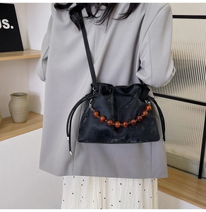 Detail of black velvet drawstring bucket bag with amber bead chain and slim strap