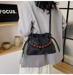 Detail of a black drawstring bucket bag with amber resin bead chain on soft leather