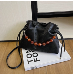 Detail of black cloud-style bucket bag with drawstrings and amber beaded chain strap