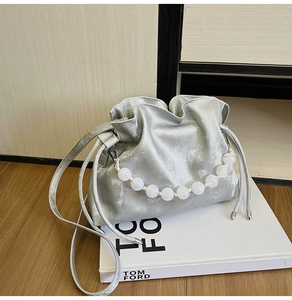 Detail of silver metallic drawstring bucket bag with elegant large white pearl handle