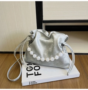Detail of silver drawstring bucket bag with large translucent beaded handle on white box