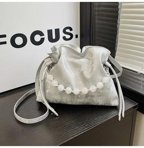 Detail of silver metallic cloud bucket bag featuring large pearl chain and drawstring