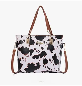 Detail of cow print tote bag featuring brown PU leather handles and gold-tone hardware