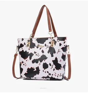 Detail view of stylish cow print tote bag featuring brown straps and gold logo hardware