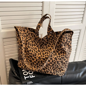 Detail of leopard print canvas tote bag featuring dual handles on black leather surface