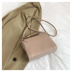 Close-up of beige faux leather handbag on white fabric with olive green blazer