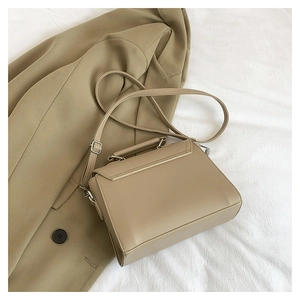 Close-up of khaki pebbled leather handbag with flap and handle on a beige blazer