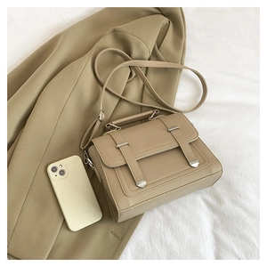 Detailed close-up of khaki leather handbag with vintage metal tips on white fabric