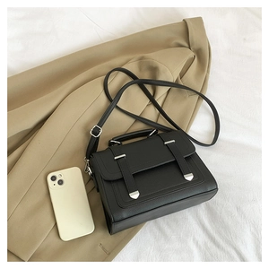Detail of black pebbled leather crossbody bag with silver accents next to a smartphone