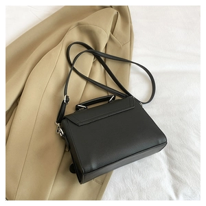 Detail of black litchi grain leather handbag with silver hardware on khaki blazer