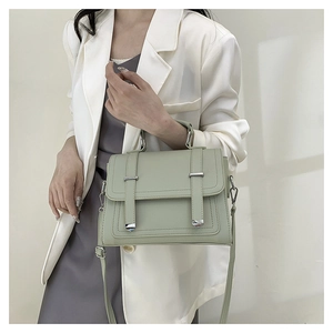 Sage green crossbody bag with top handle shown on a model in a minimalist white suit