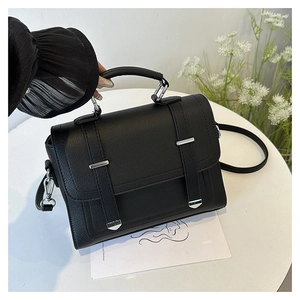 Close-up of black litchi pattern leather handbag with silver hardware on a white table