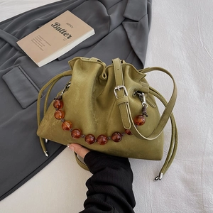 Olive green drawstring bucket bag with amber beaded chain on white linen background