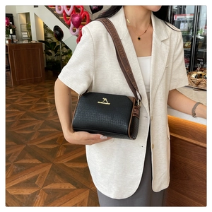 Detail of black embossed leather crossbody bag with gold logo and wide fabric strap