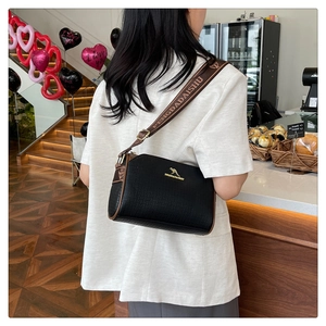 Detail of black lychee grain leather bag with brown textile strap and gold kangaroo logo