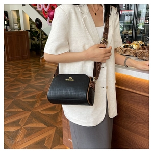 Detail of black textured crossbody bag with gold logo and wide patterned strap