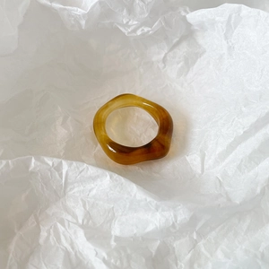 Detailed view of an irregular amber resin ring with a natural wavy texture on white paper