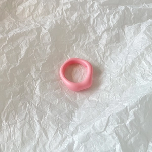 Detail of pink resin ring with wide irregular wave design on white textured background