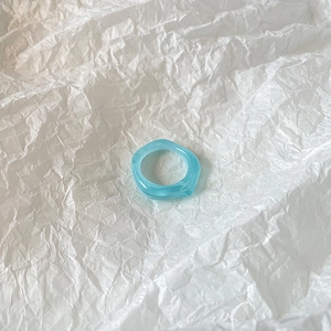 Macro view of light blue resin ring with irregular wavy design on white paper
