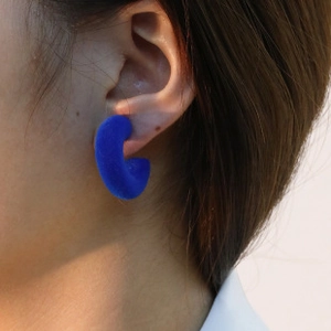 Detail of Klein blue flocked C-shaped earrings worn by a model in a close-up profile view
