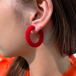Close-up of red flocked hoop earring on model showing velvet texture and round design