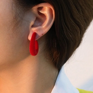Close-up of a red flocked C-shaped earring with velvet texture worn by a model