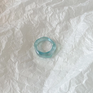Detail of light blue transparent resin ring with an irregular wave design on white paper