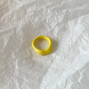 Macro shot of minimalist bright yellow irregular resin ring on white textured paper