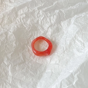 Close-up of a vibrant orange resin geometric ring on a textured white background