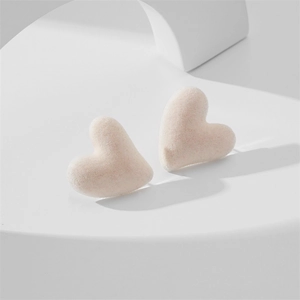 Detailed macro view of soft pink flocked heart stud earrings on a geometric stand