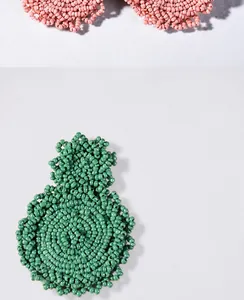 Macro shot of handmade beaded earrings in green and pink with detailed woven textures