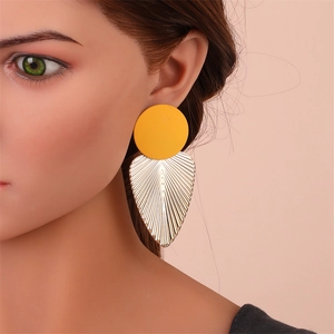 Gros plan de boucles d'oreilles bohèmes avec clou jaune mat et pendentif feuille dorée