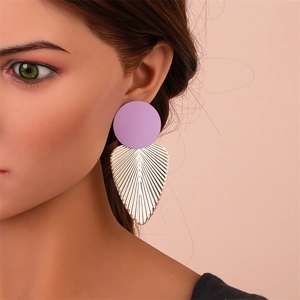 Vue macro de boucles d'oreilles rondes mates violettes et feuilles dorées sur modèle