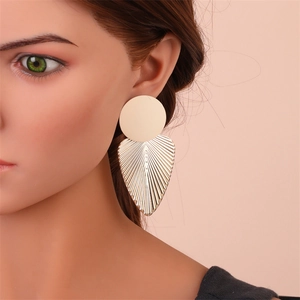Détail de boucles d'oreilles feuilles dorées oversize avec texture brossée sur l'oreille