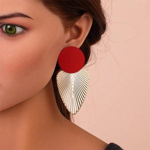 Détail d'un clou d'oreille rouge et d'un pendant feuille dorée porté par mannequin