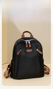 Detail of black nylon backpack featuring brown leather handle and silver metal zipper accent