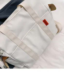 Close-up of white nylon tote bag with wide straps and brown leather detail on the shoulder strap