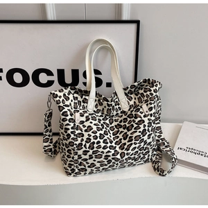 Detail of leopard print tote bag featuring cream straps and metallic buckles on white surface