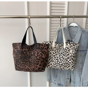 Detail view of large leopard print canvas tote bags with leather handles on a display rack